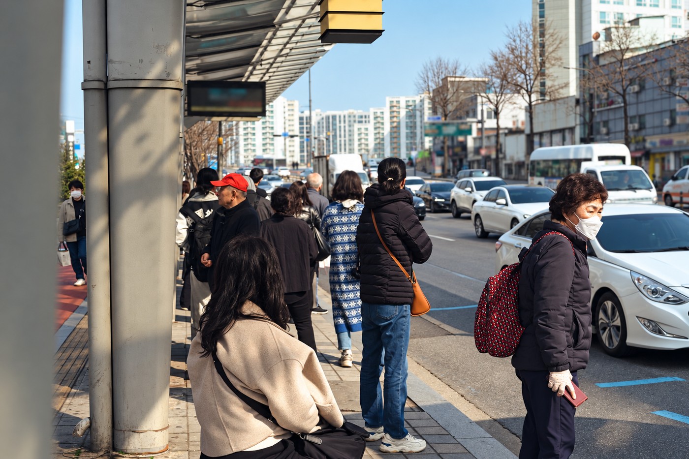 Passengers waiting beside a bus shelter on a Seoul street