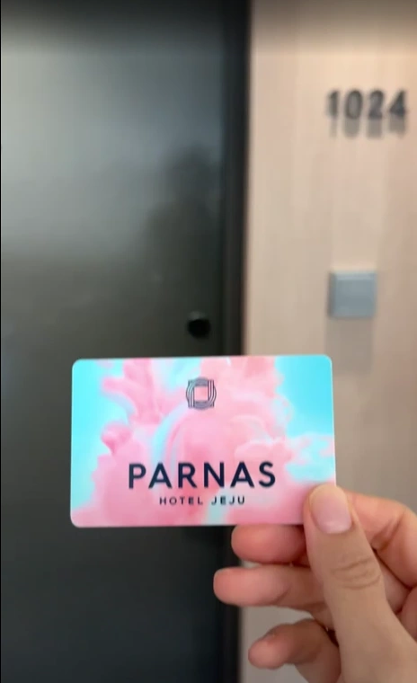 A hand holding a Parnas Hotel Jeju key card in front of a room door