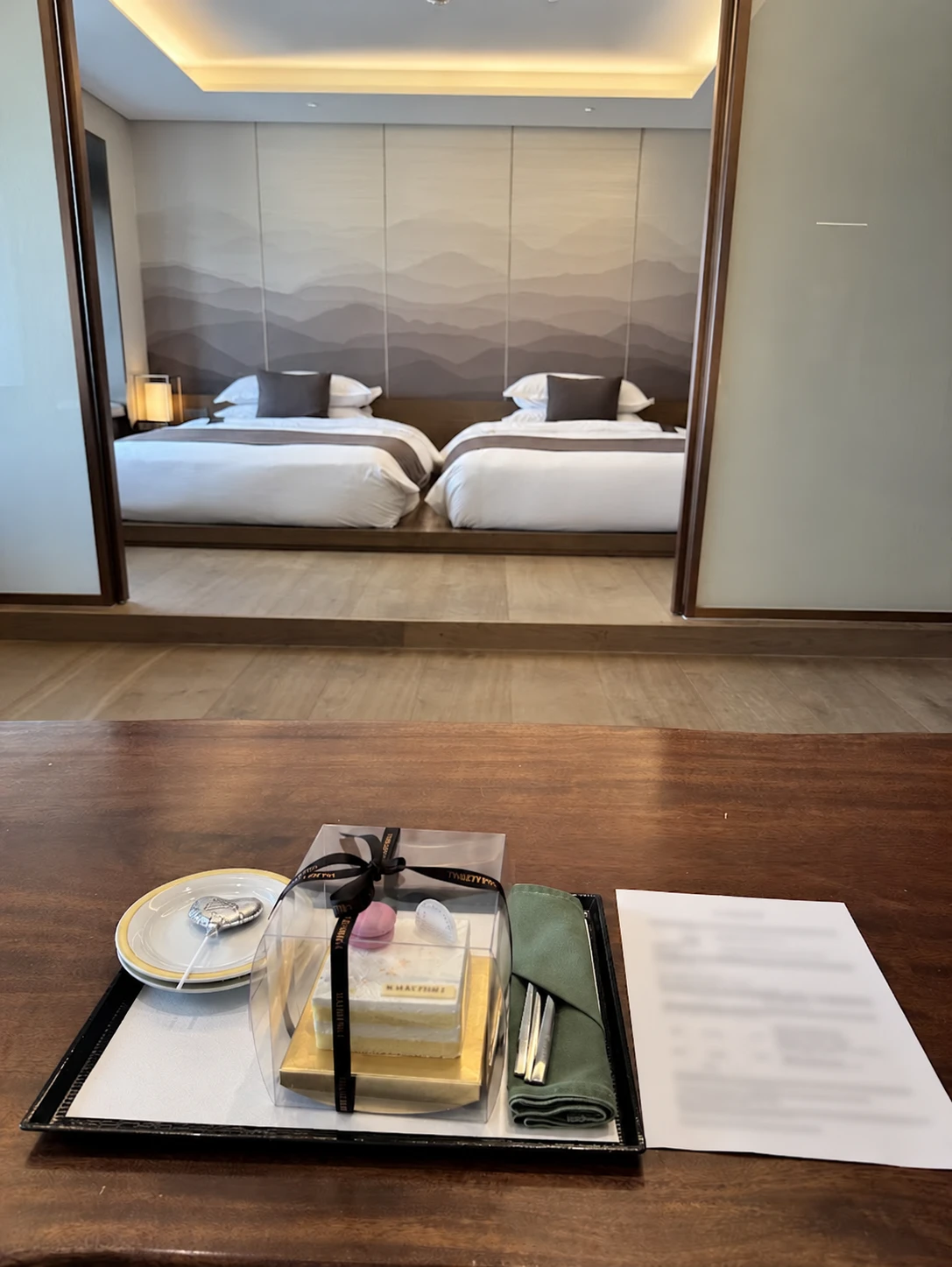 Twin beds beyond a desk with a cake and an information sheet