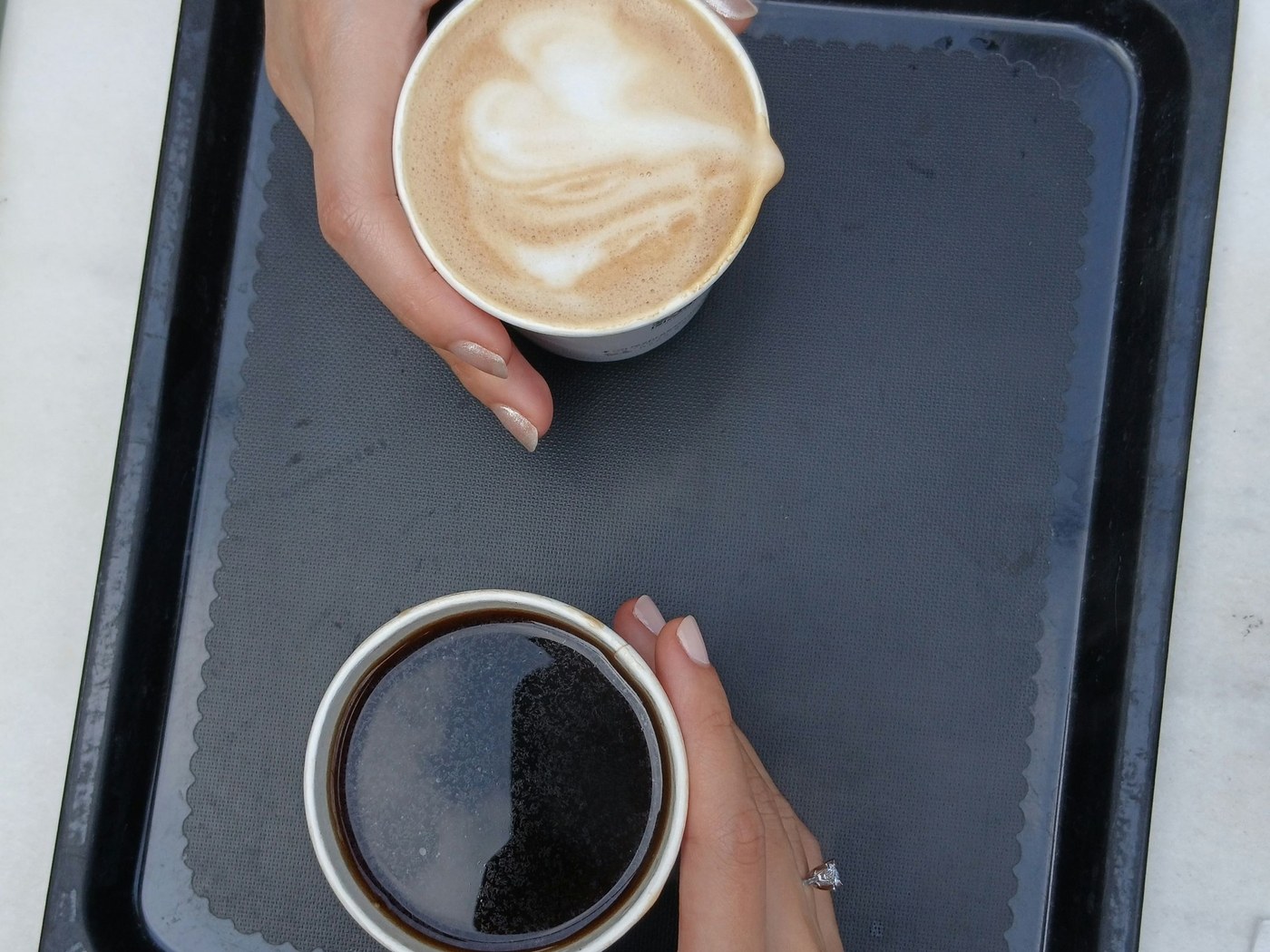 Two hands holding coffee cups over a dark tray