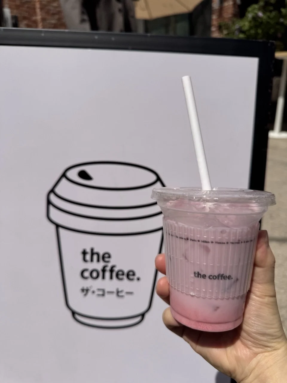 A pink iced drink in a The Coffee cup beside the cafe logo sign in Seongsu.